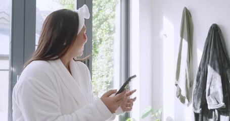 Receiving phone alert, Asian woman laughing at phone, admiring garden by glass doors, copy space - Powered by Adobe