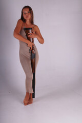 Slender barefoot young woman in long dress holding double barrelled vintage shotgun on grey background full length