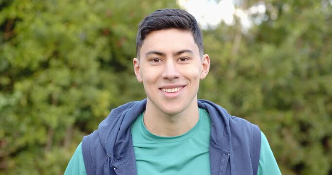 Man smiling gradually and then chuckling before leaning back and laughing openly in leafy garden
