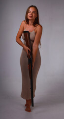 Beautiful young woman in grey dress aiming with vintage shotgun on grey background