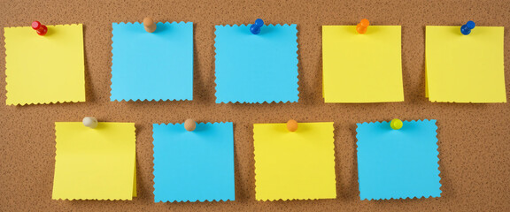 Pinned yellow and blue notes on corkboard with vibrant pushpins. Organized workspace ideal for reminders, planning, and educational content themes