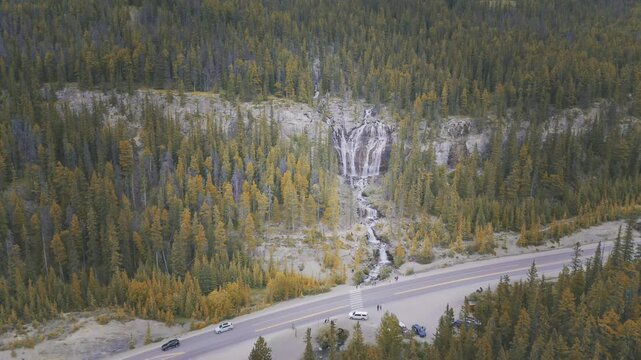 Icefields parkway with a stunning waterfall cascading through autumn-colored trees in Alberta