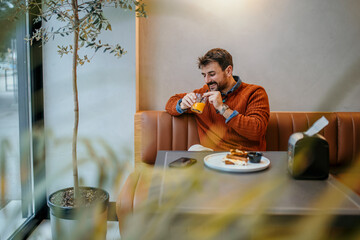 Happy man enjoying breakfast with orange juice in cozy cafe