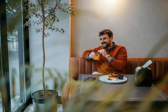 Happy man enjoying breakfast with orange juice in modern cafe - Powered by Adobe