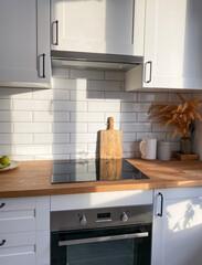 Stylish kitchen with electric stove, wooden countertop and white cabinets, filled with morning natural light.