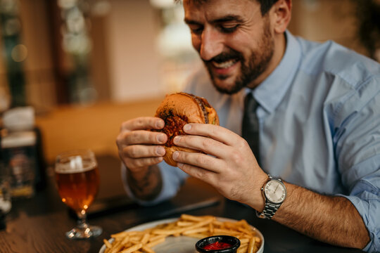 Happy businessman enjoying burger and french fries in restaurant - Powered by Adobe