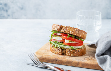 Sandwich of grain bread with fresh tomatoes mozzarella, arugula and pesto on a wooden board