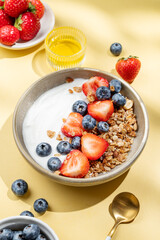 Natural yogurt with granola, blueberry and strawberry in a bowl on a bright yellow background