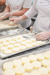 Chefs in uniform prepare cottafe cheese or syrniki on metal trays sprinkled with flour in a bakery kitchen.
