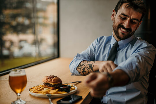 Happy businessman rolling up sleeves before eating burger and fries in restaurant - Powered by Adobe