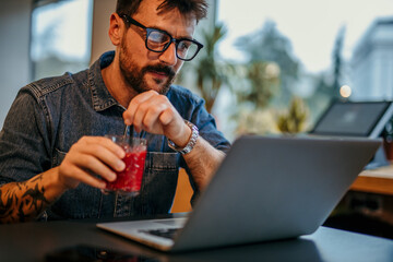 Focused freelancer enjoying a refreshing drink while working on laptop