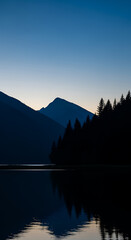 Serene Mountain Lake Reflection at Dusk with Silhouetted Evergreen Trees