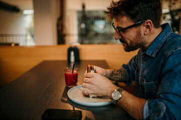 Young man enjoying a sandwich and juice at a modern cafe