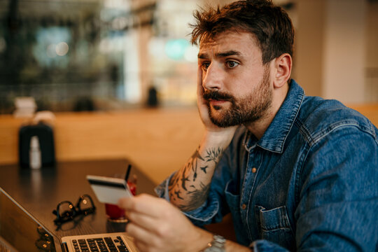Pensive man making online payment holding credit card in cafe
