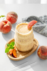 Smoothie with peach and banana in a glass on a wooden board on a white table near window