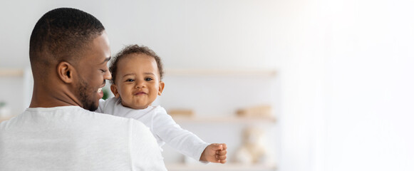 Baby Insurance. Young Black Father Holding Cute Smiling Infant Child On Hands At Home, Adorable Little African American Kid Smiling At Camera, Enjoying Time With His Daddy, Panorama With Copy Space