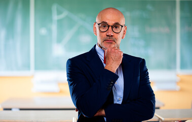 Portrait of senior male professor standing in front of chalkboard at school