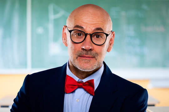 Portrait of senior male professor standing in front of chalkboard at school