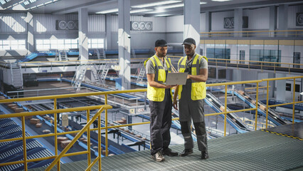 Diverse African and Multiethnic Arab Men Using Laptop Computer to Manage Automated Conveyor Belt Load, Prepare Online Shopping Orders for Delivery. Warehouse Associates Having a Conversation at Work