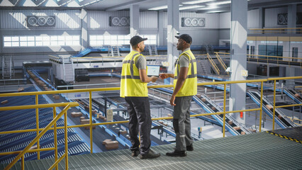 Diverse African and Multiethnic Arab Men Using Laptop Computer to Manage Automated Conveyor Belt Load, Prepare Online Shopping Orders for Delivery. Warehouse Associates Having a Conversation at Work