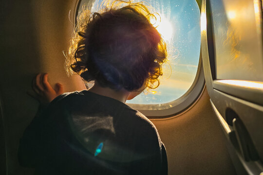 A child looking to the sunset through the window of an airplane