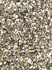Close-up top view of a natural gravel surface with a mix of small pebbles and stones in various colors and shapes. 