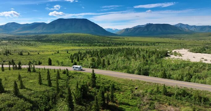 Travelling by the wilderness of stunning Alaska. A campervan moves by the road in the valley surrounded by the mountains.