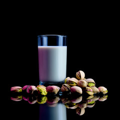 Glass of pistachio milk with whole pistachios on reflective surface against black background, clean studio shot perfect for vegan, food, product branding. dairyfree, green, protein, nutrition, organic