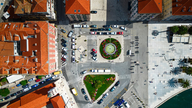 Aerial view of a vibrant square featuring a circular fountain and a triangular green space, surrounded by terracotta rooftops and bustling streets, Split, Split-Dalmatia County, Croatia.