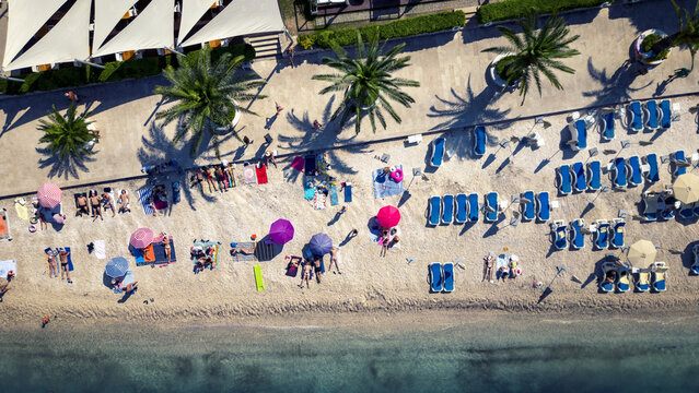 Aerial view of sunbathers dotting the beach with vibrant umbrellas under the shade of palm trees, Split, Split-Dalmatia County, Croatia.