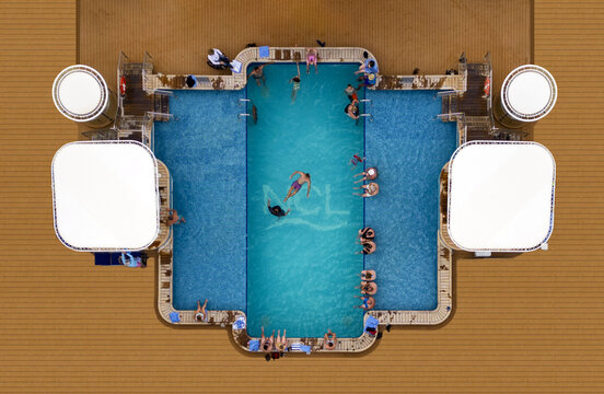 Aerial view of a vibrant blue swimming pool surrounded by sunbathers and white canopies, creating a striking contrast against the warm deck, Split, Split-Dalmatia County, Croatia.