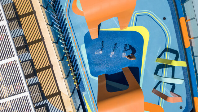 Aerial view of bright orange and cool blue shapes create dynamic contrasts over the splash pad, where a lone figure plays among the water features, Split, Split-Dalmatia County, Croatia.