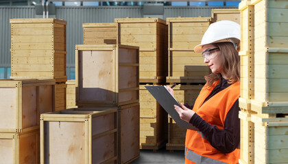 Female worker with clipboard inspects stacked wooden crates in outdoor storage area, ensuring inventory control and logistics accuracy. Warehouse, Logistics, Inventory, Customs.