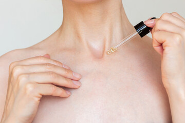 A young woman applying a moisturizing serum from a pipette to the skin of the neck and decollete. Wrinkle prevention and skin care
