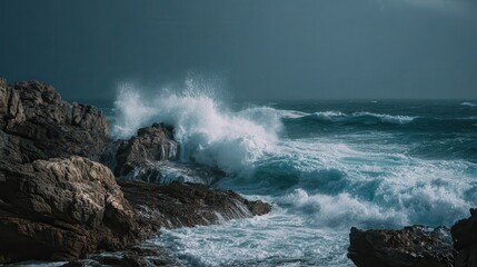 Waves crash against rocky cliffs at a coastal location under a dramatic sky during an overcast day