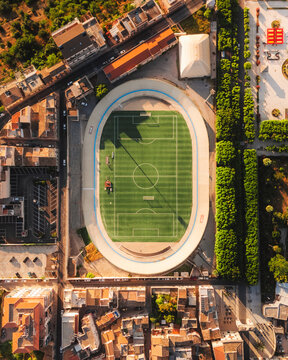 Aerial view of the stadium, a vibrant green island surrounded by the city's terracotta rooftops, bathed in the warm glow of the sun, Noto, Sicily, Italy.