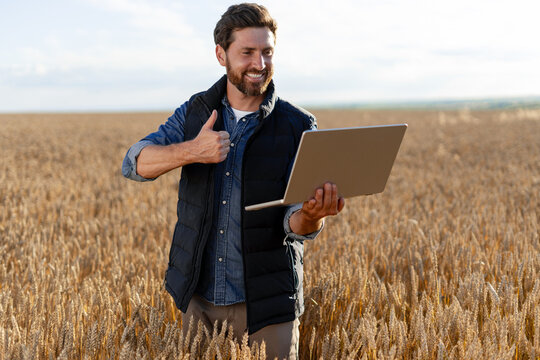Farmer holding laptop and showing thumbs up in wheat field