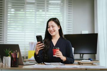 A smiling young woman reviews documents at her desk, with a laptop, calculator, and graphs on a...
