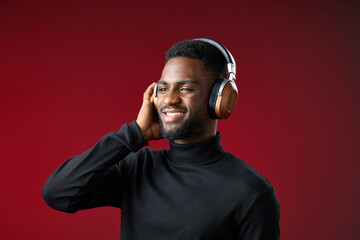 Smiling man in a black turtleneck wearing headphones, enjoying music with a vibrant red background, reflecting joy and modern lifestyle