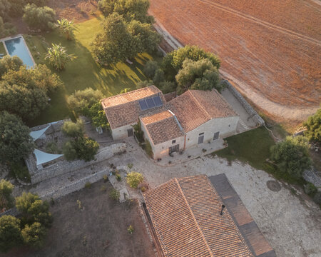 Aerial view of a sun-drenched Rifugio Lanzagallo estate, where rustic buildings meet manicured greenery against a backdrop of golden fields, Ispica, Sicilia, Italy.