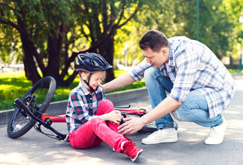 Fototapeta premium Attentive Dad Is Comforting His Daughter After Bike Accident, checking on her leg