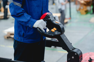 Worker in blue uniform and gloves operating electric pallet jack in cardboard packaging factory