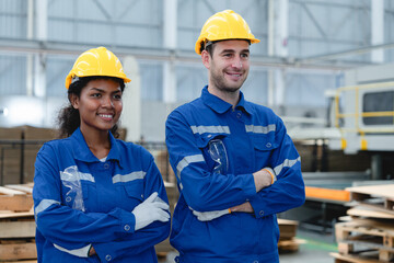 Portrait of diverse industrial workers in hard hats confidently standing with arms crossed in warehouse environment