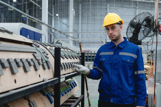 Male technician in blue uniform with yellow helmet inspects rotary die-cut mold used in corrugated box production, emphasizing machinery maintenance and industrial precision.