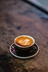 Cup of cappuccino with intricate latte art, served on a rustic wooden table in a cozy coffee shop setting. Warm and inviting atmosphere, perfect for a relaxing coffee moment, captured in natural light