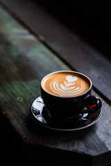 Cup of cappuccino with intricate latte art, served on a rustic wooden table in a cozy coffee shop setting. Warm and inviting atmosphere, perfect for a relaxing coffee moment, captured in natural light