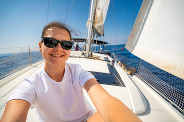 Happy young woman sitting on the bow of a sailing yacht with full sails near Croatia. Freedom, adventure, summer lifestyle and slow travel at sea.