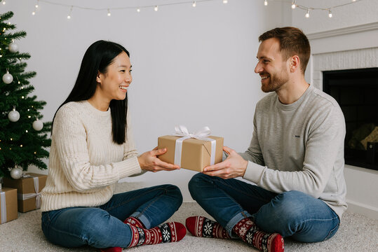 young interracial couple exchanging gifts near christmas tree in cozy living room celebrating holiday season