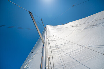 Full white sails blown by the wind against blue sky during sailing near Croatia. Symbol of movement, freedom and summer maritime journey.