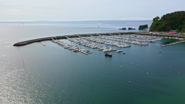 Vertically tilted approaching drone movement to the Morgat marina with moored yachts and sailboats lined up, Crozon, Brittany, France.